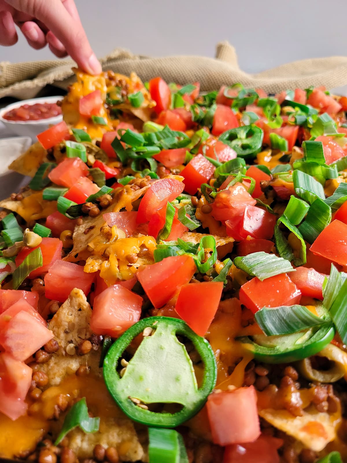 hand lifting a tortilla chip off a tray of loaded lentil nachos