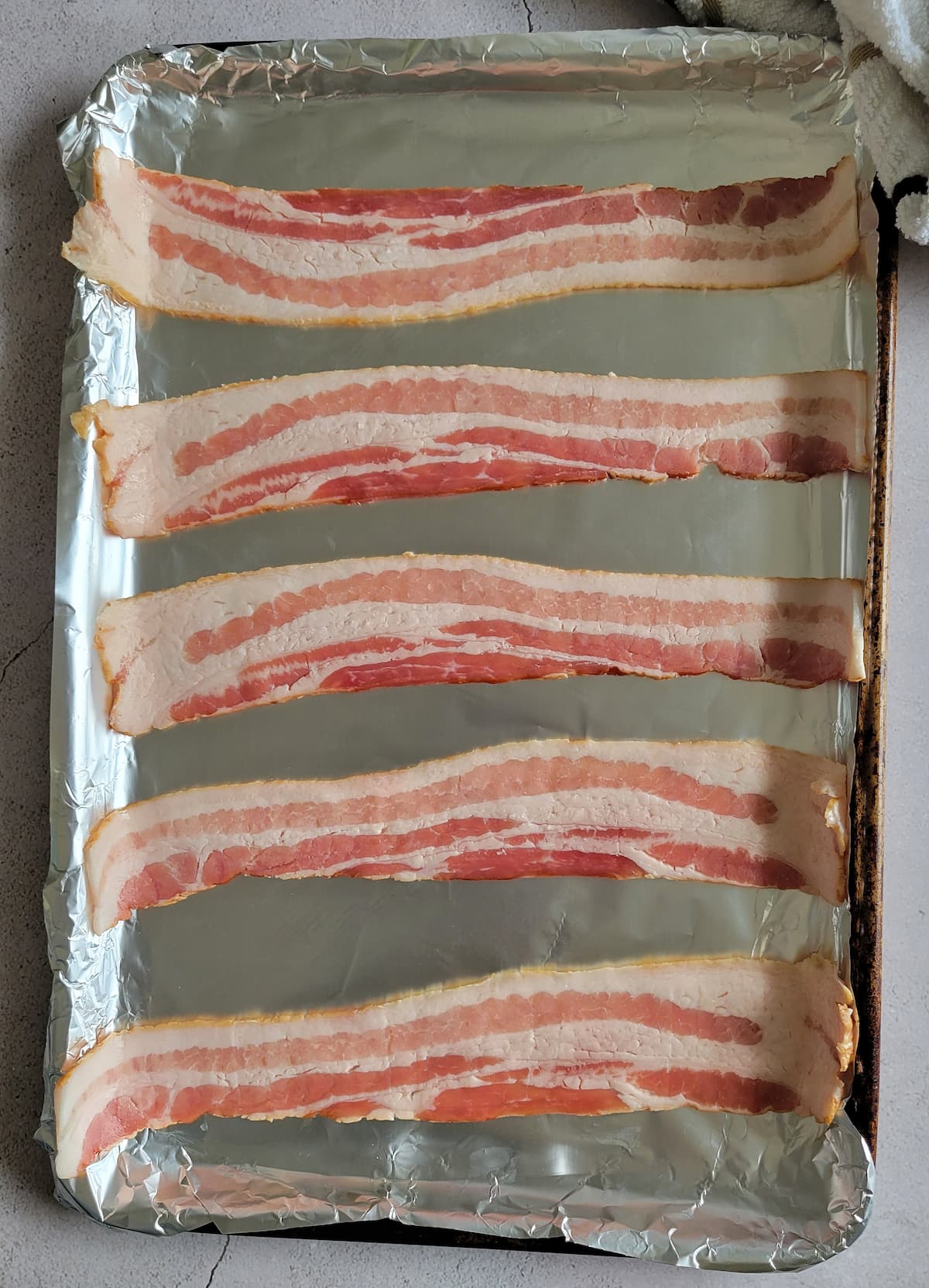5 strips of raw bacon on a foil lined baking sheet