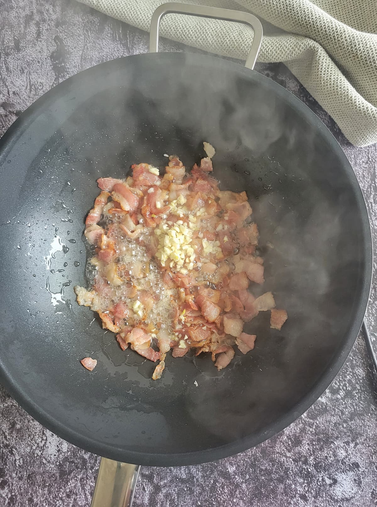 diced bacon cooking in a wok with a pile of minced garlic on top