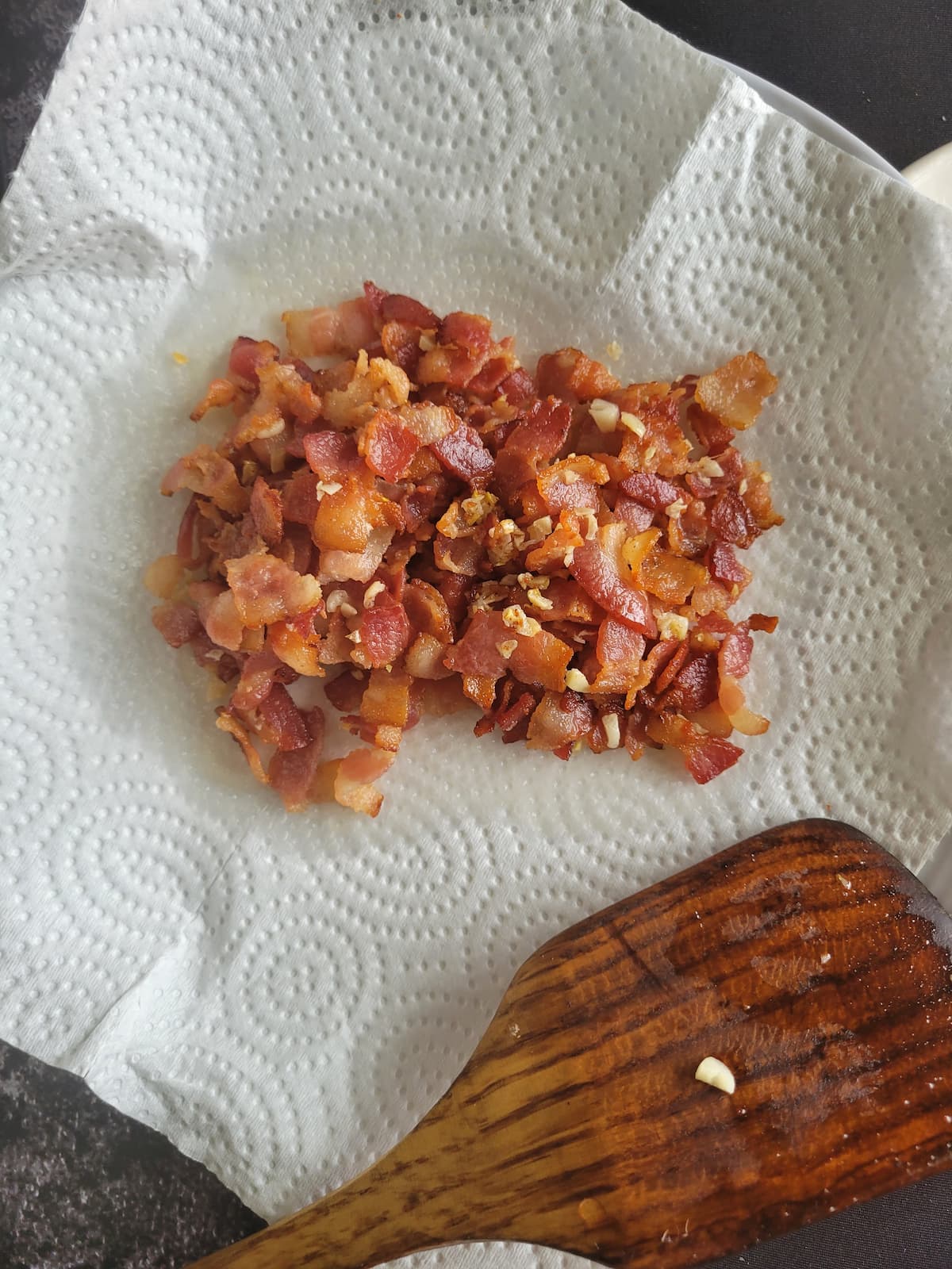 cooked bacon and garlic on a paper towel lined plate with a wooden spatula