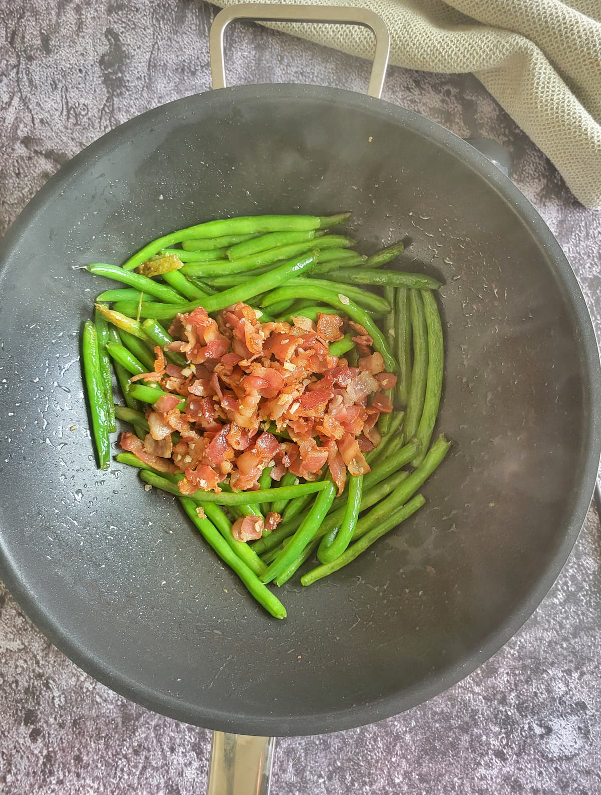green beans in a wok with a pile of cooked crumbled bacon on top