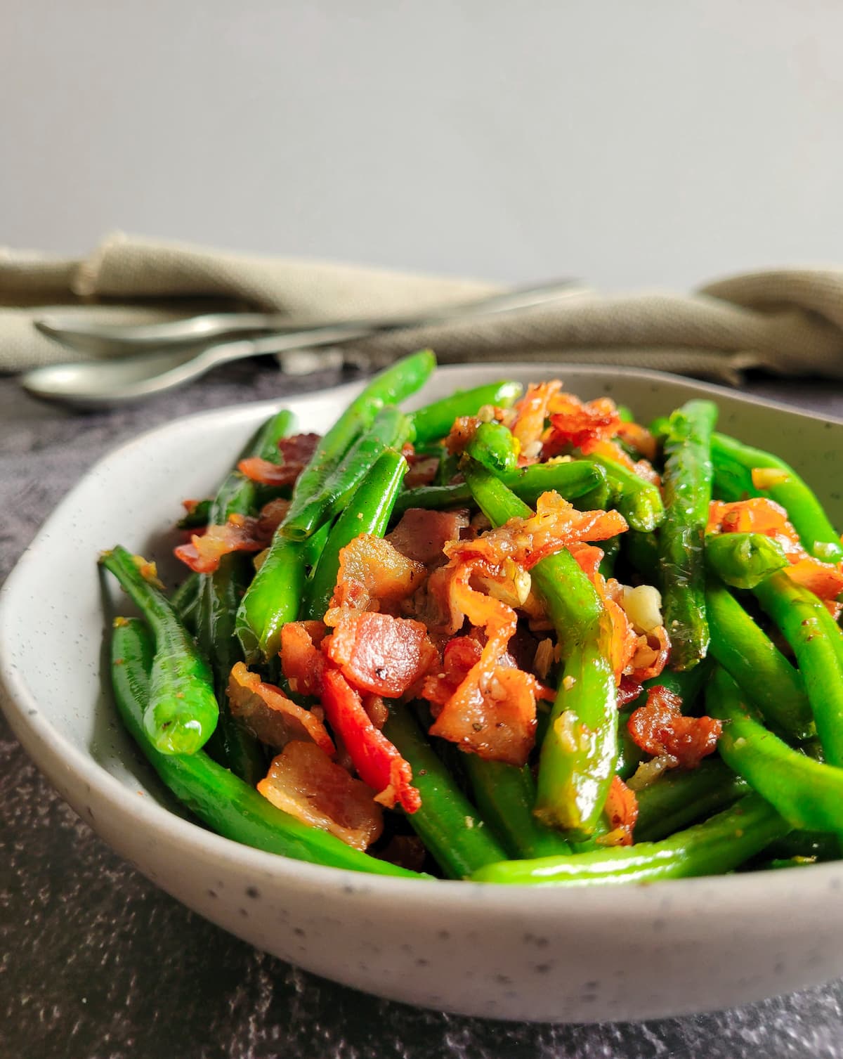 green beans and bacon in a bowl, two spoons in the background