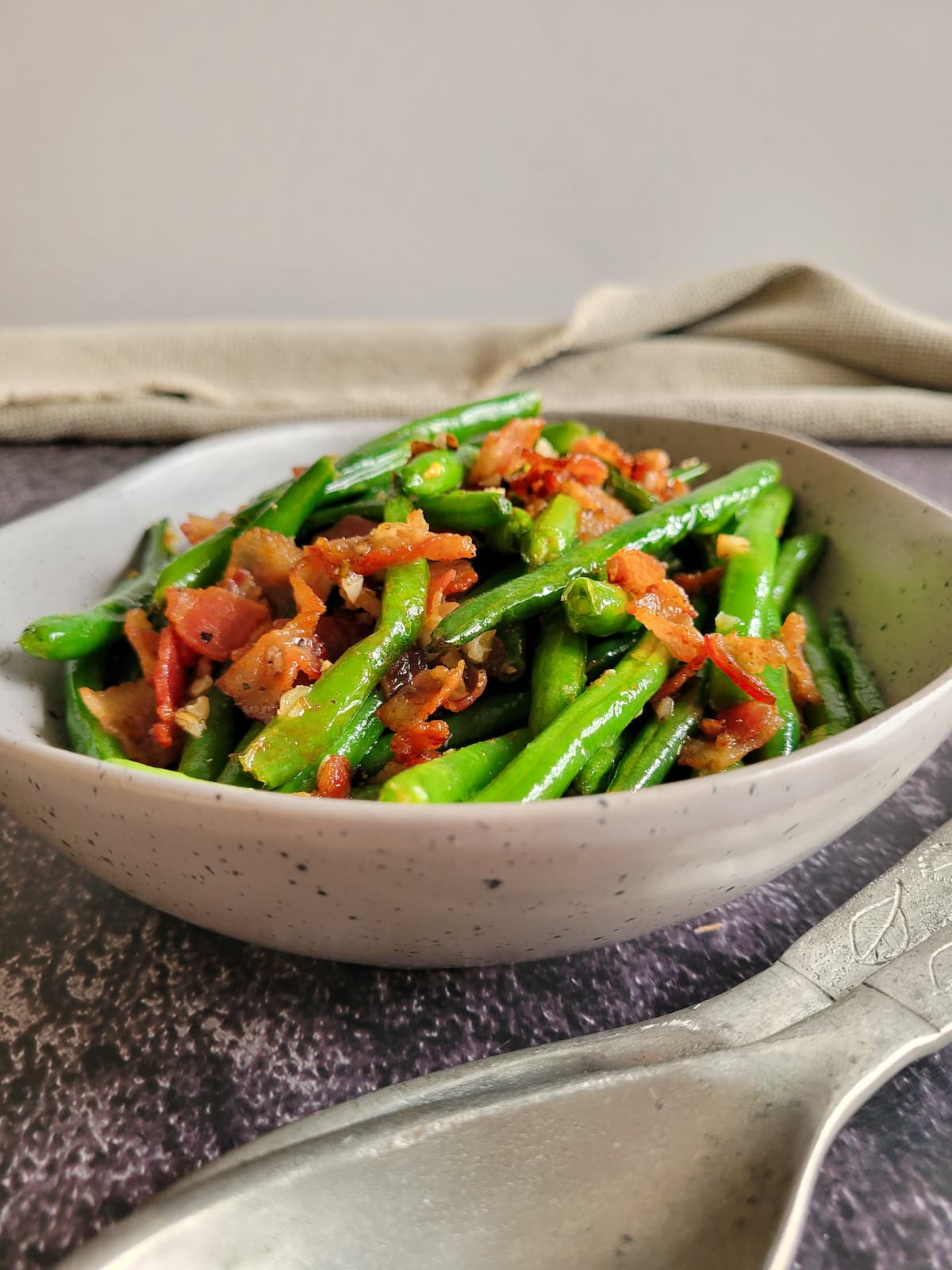 bowl of bacon with green beans, two spoons in the front