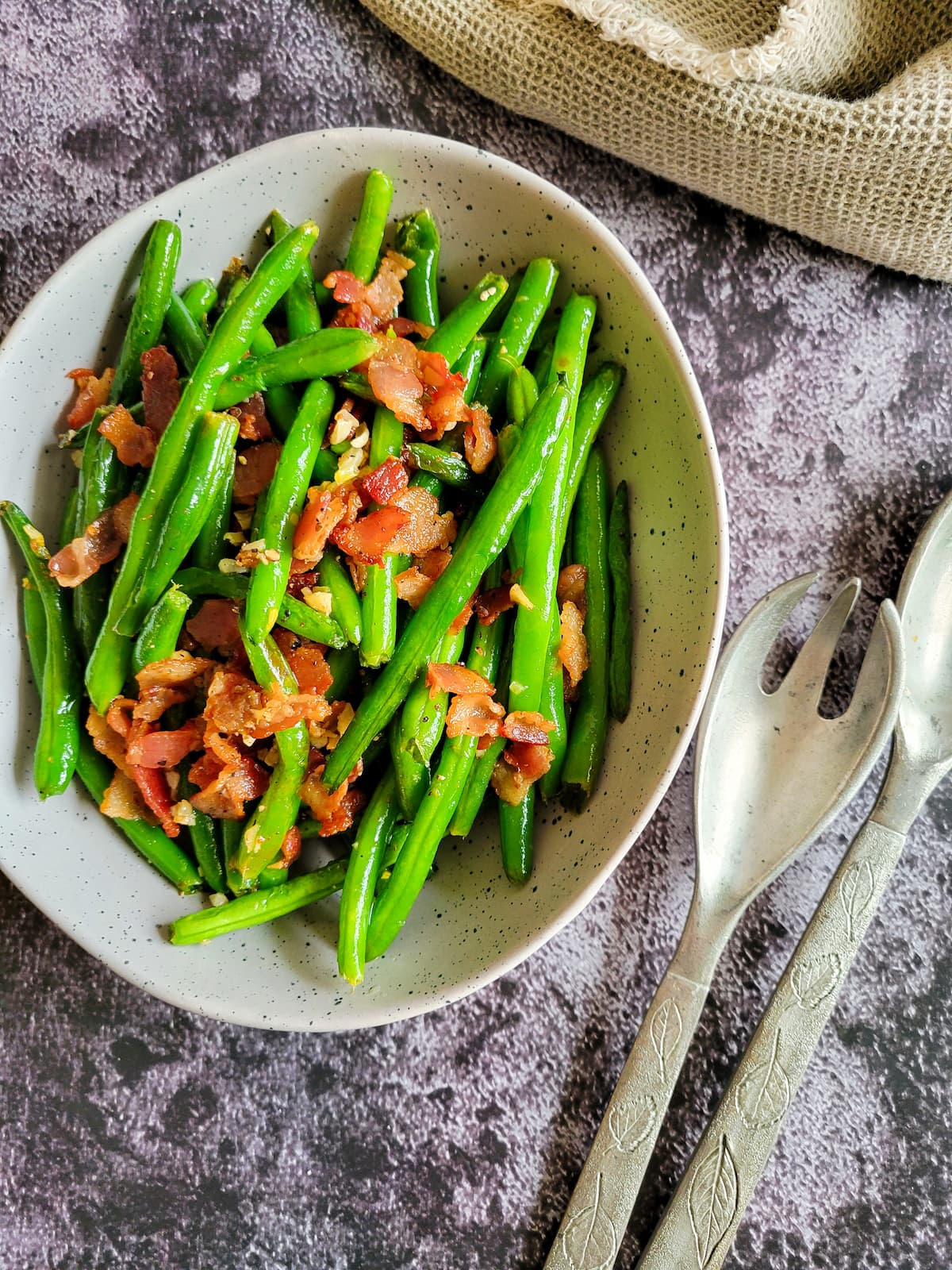 bowl of bacon, green beans and garlic next to serving spoons
