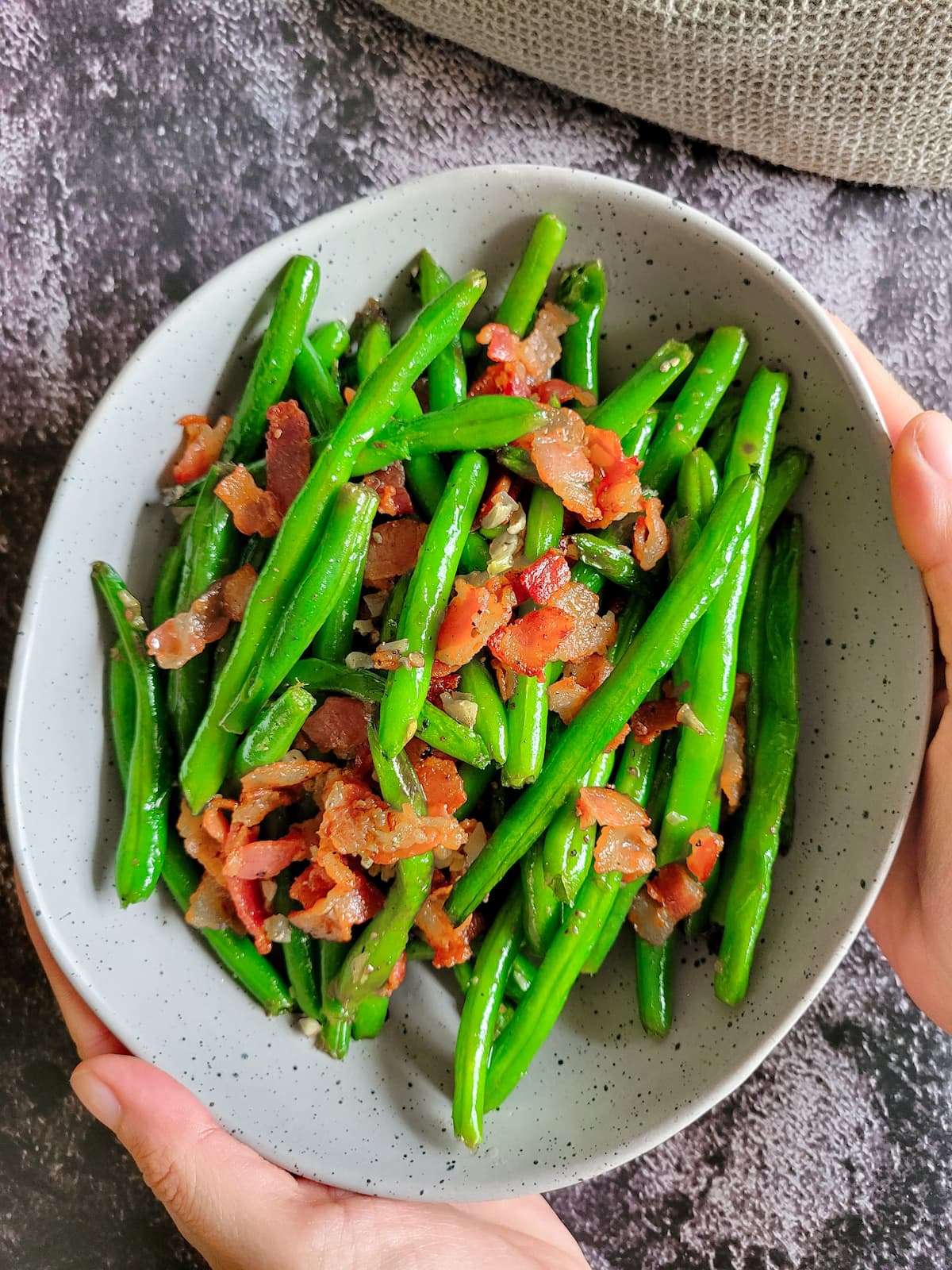 hands holding a bowl of bacon and green beans