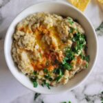 bowl of baba ganoush topped with fresh chopped parsley, olive oil and smoked paprika, tortilla chips and more fresh parsley around it