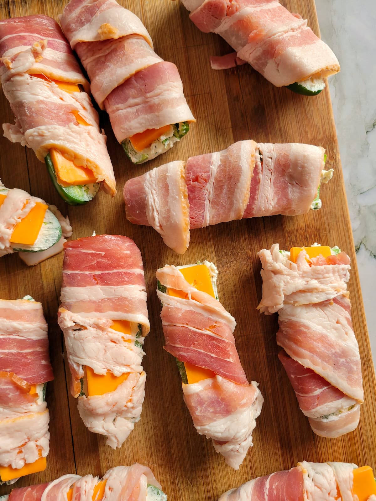 raw bacon wrapped jalapeno poppers on a cutting board