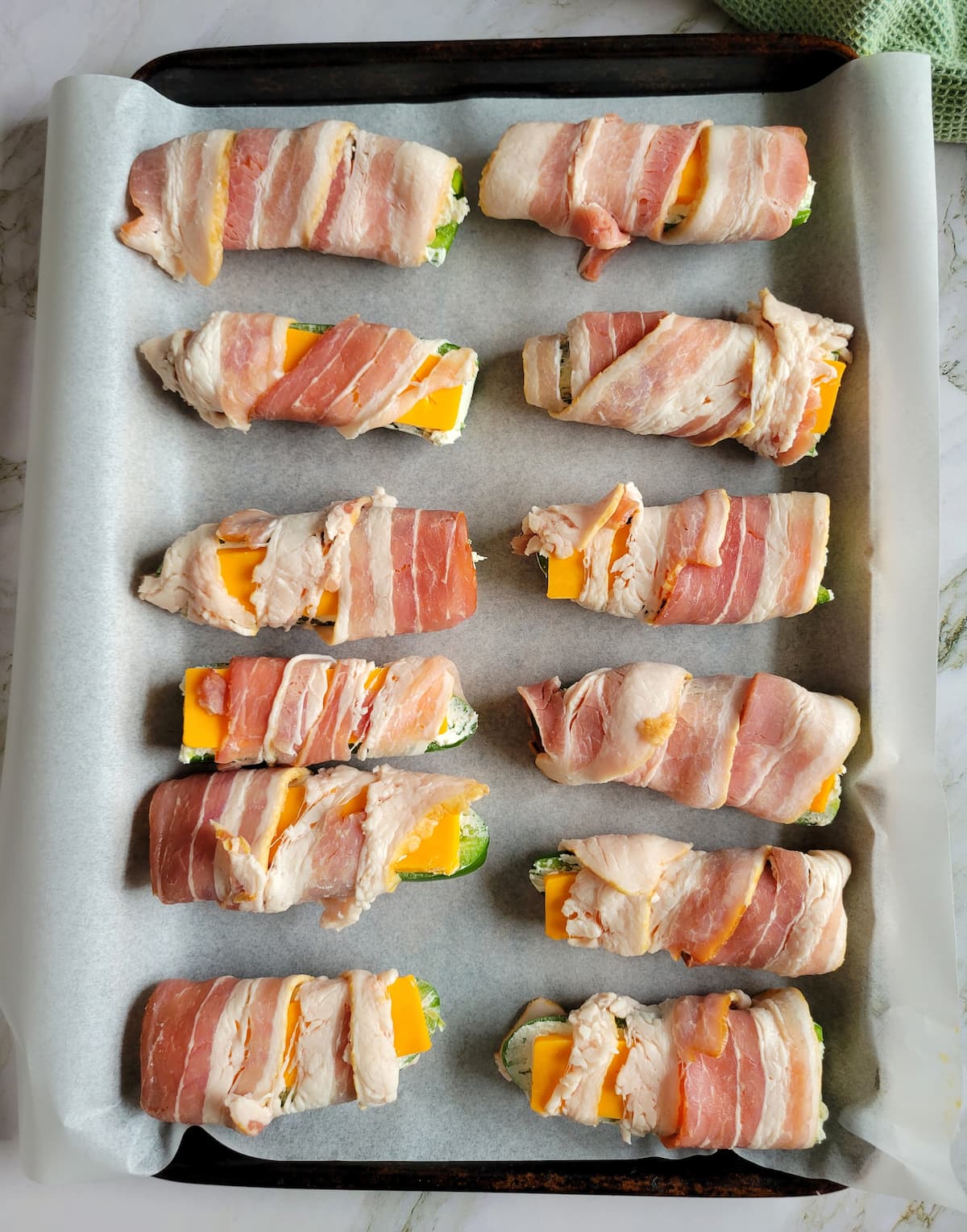 raw bacon wrapped jalapeno poppers on a parchment lined baking sheet