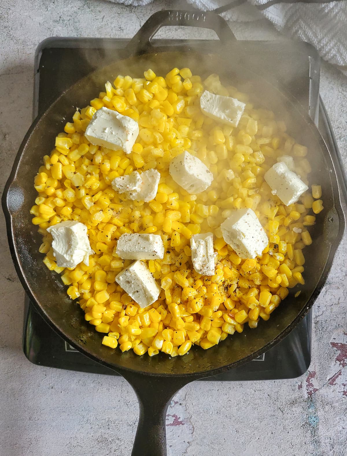 kernels of corn with chunks of cream cheese steaming in a cast iron skillet on a burner