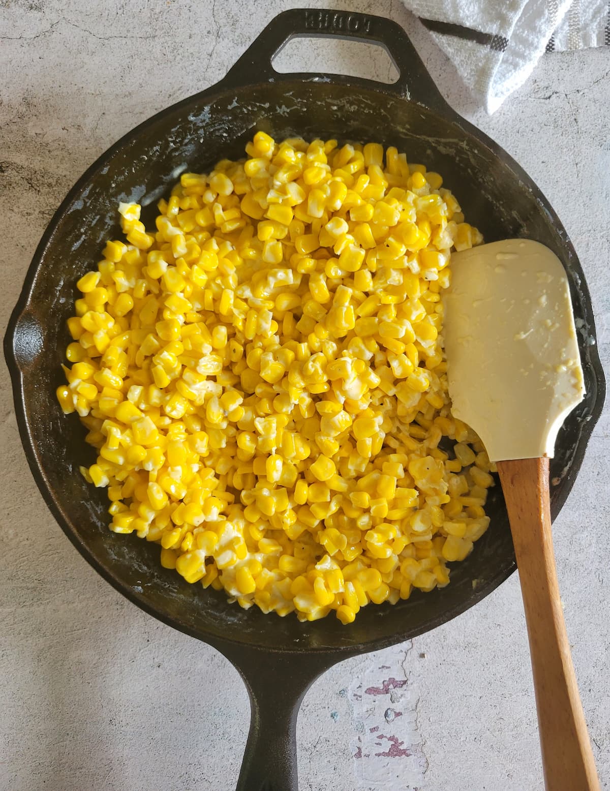 creamy corn in a cast iron skillet, rubber spatula in the pan