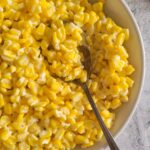 A white bowl of cream cheese with corn with a spoon in it.