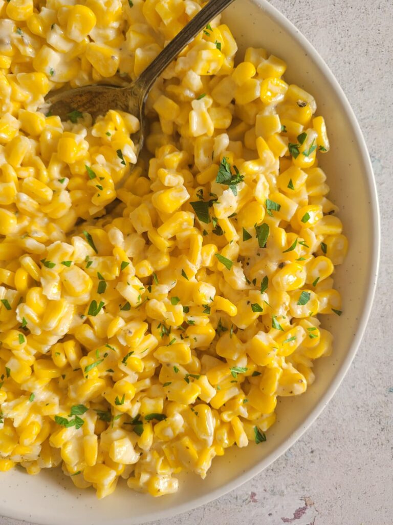 bowl of creamy corn with a spoon it it, garnished with fresh chopped parsley