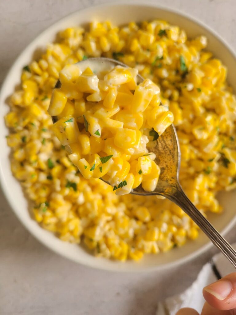 spoonful of creamy corn garnished with fresh chopped parsley over a bowl with the rest of it