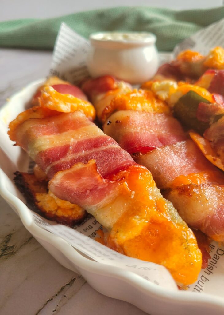 jalapeno poppers wrapped in bacon with cheddar cheese in a bowl with a white dipping sauce in the background