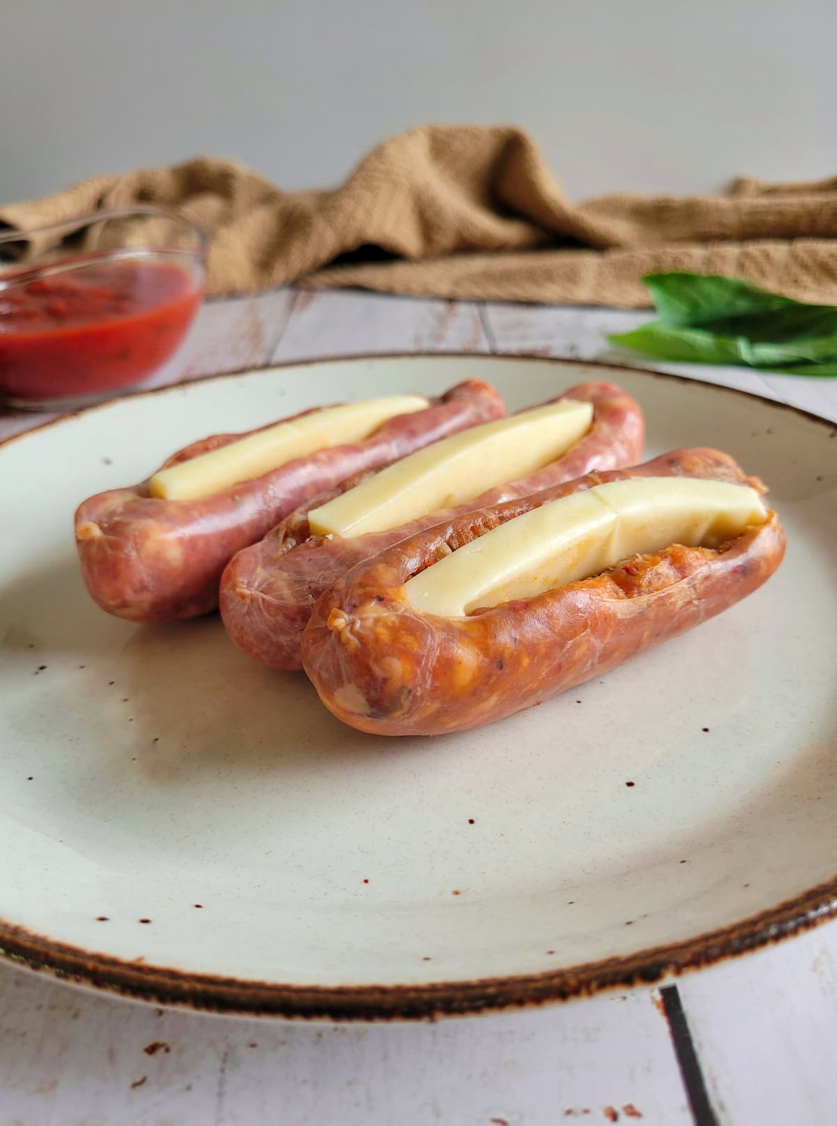 3 raw sausage with mozzarella cheese in the middle on a plate, tomato sauce and fresh basil in the background