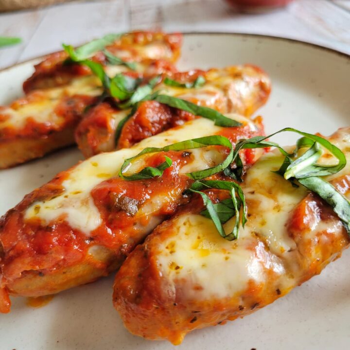 sausage stuffed with melted cheese and tomato sauce, topped with fresh basil on a plate, tomato sauce in the background