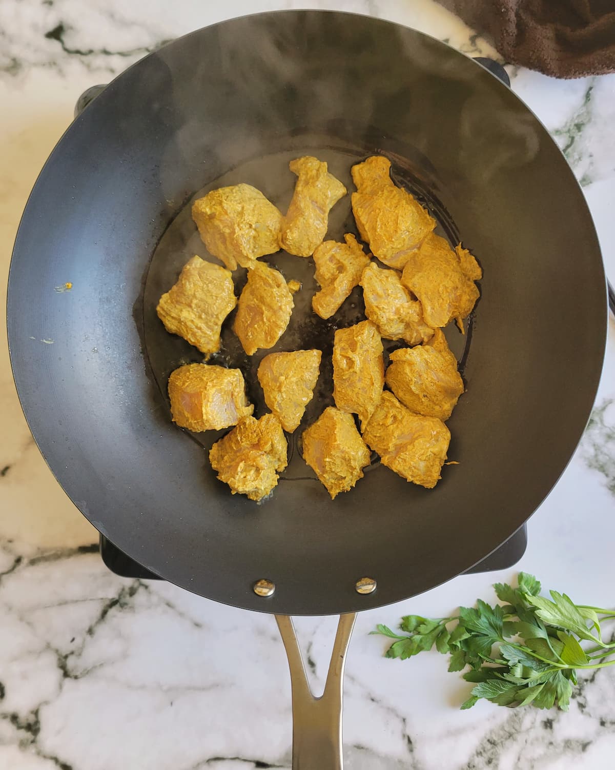 yellow seasoned chicken cubes steaming in a pan on a burner