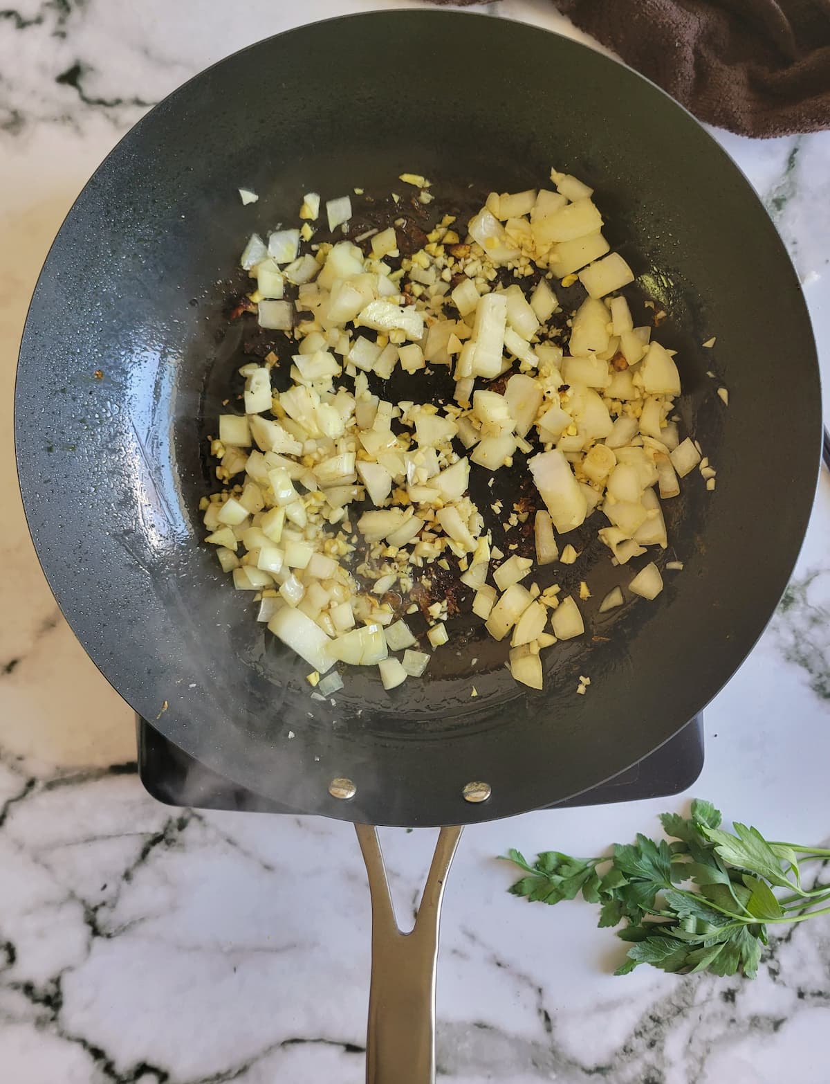 diced white onion, minced garlic and ginger in a pan on a burner