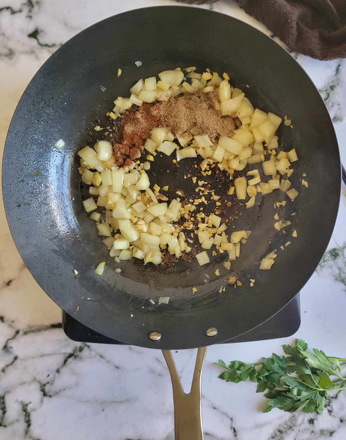 diced white onion, minced garlic, ginger and spices in a pan on a burner