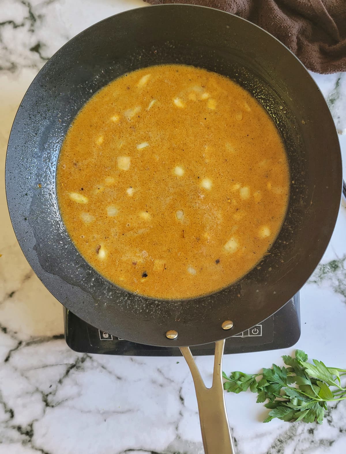 watery orange sauce with diced onions in a pan on a burner