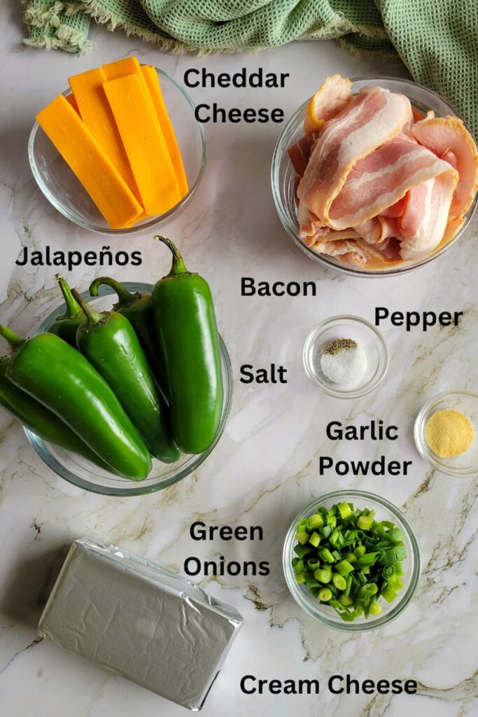 ingredients for jalapeno poppers wrapped in bacon - jalapenos, cheddar cheese, cream cheese, bacon, green onions, garlic powder, salt and pepper