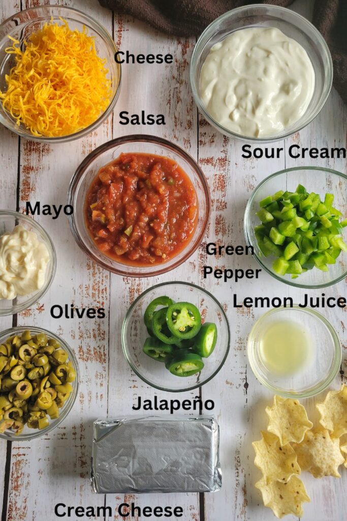 ingredients for recipe for nacho dip - sour cream, cream cheese, cheese, mayo, lemon juice, green pepper, olives, jalapeno, salsa