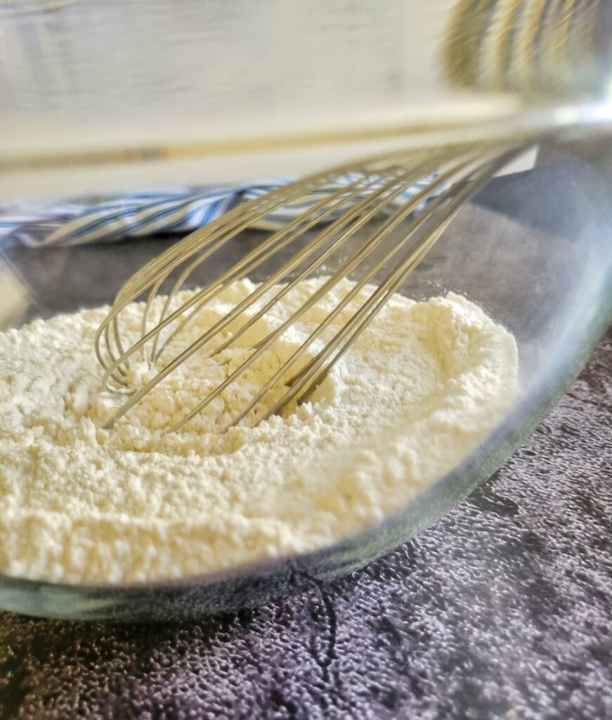 side view of a whisk in a bowl of flour