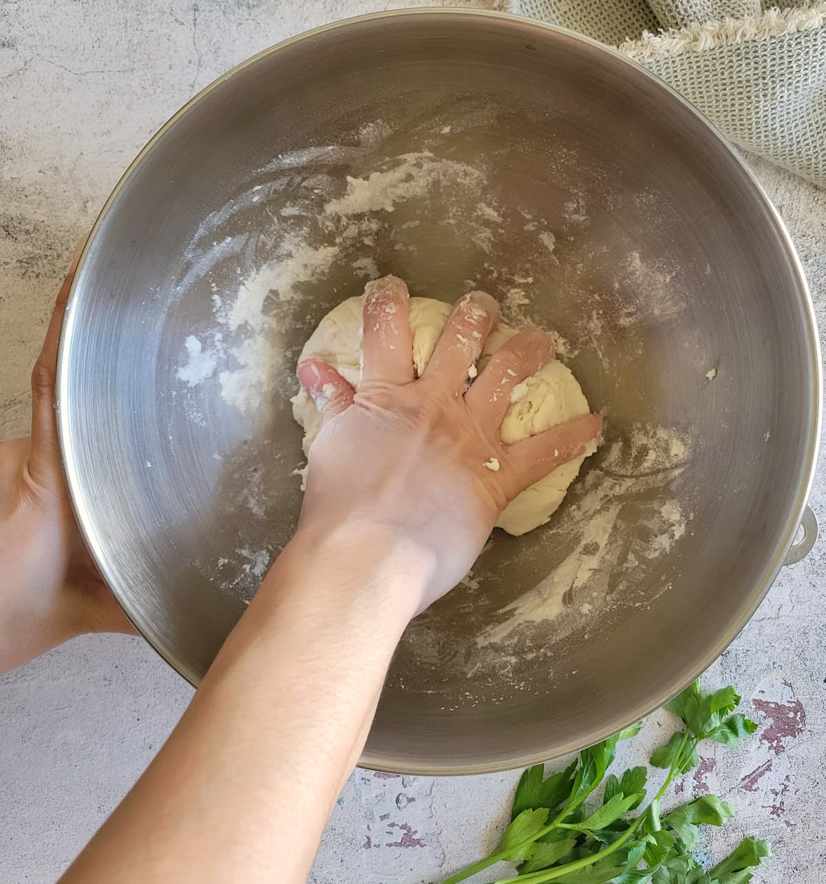 hand kneading a ball of dough in a bowl