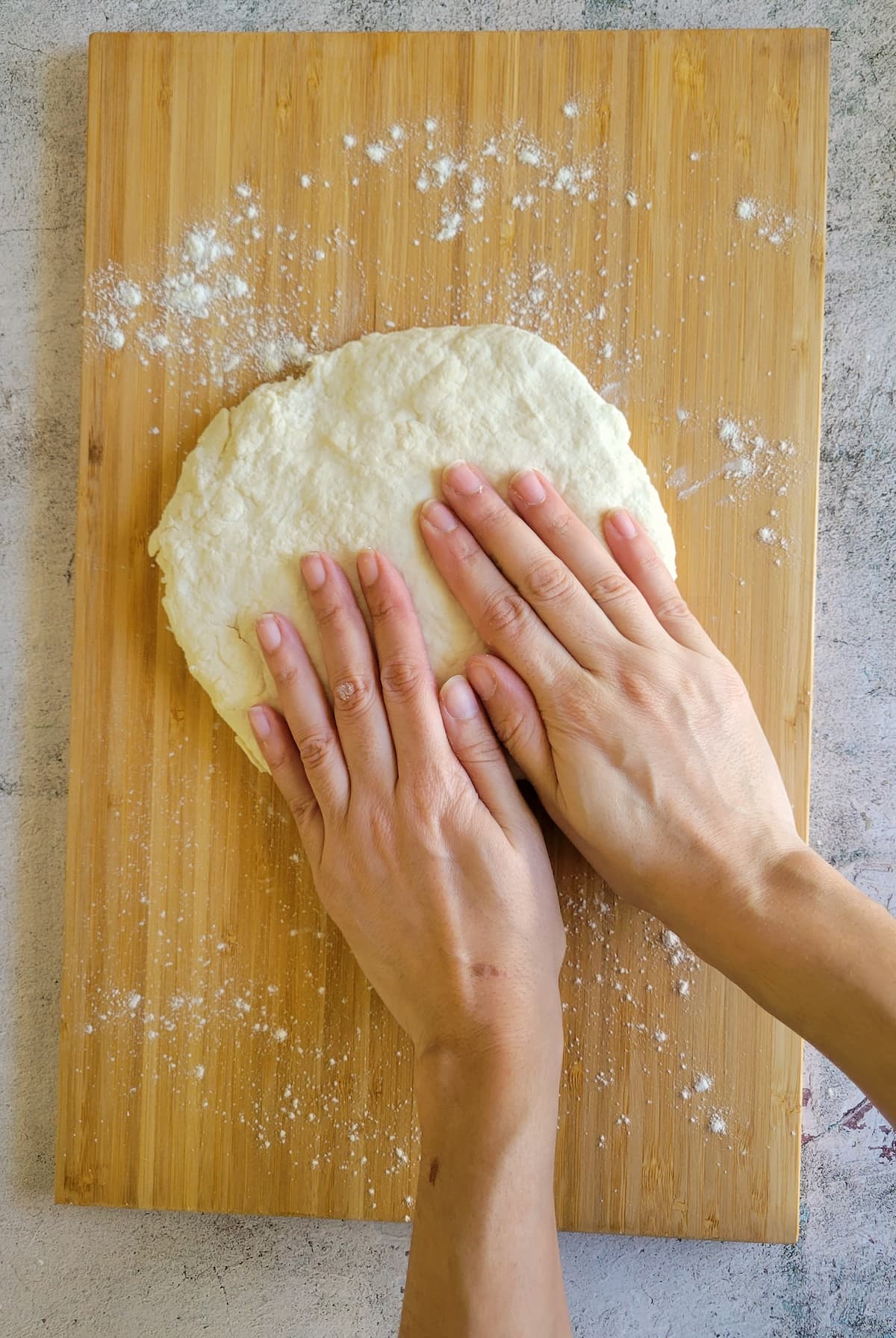 hands flattening a circular piece of dough on a cutting board