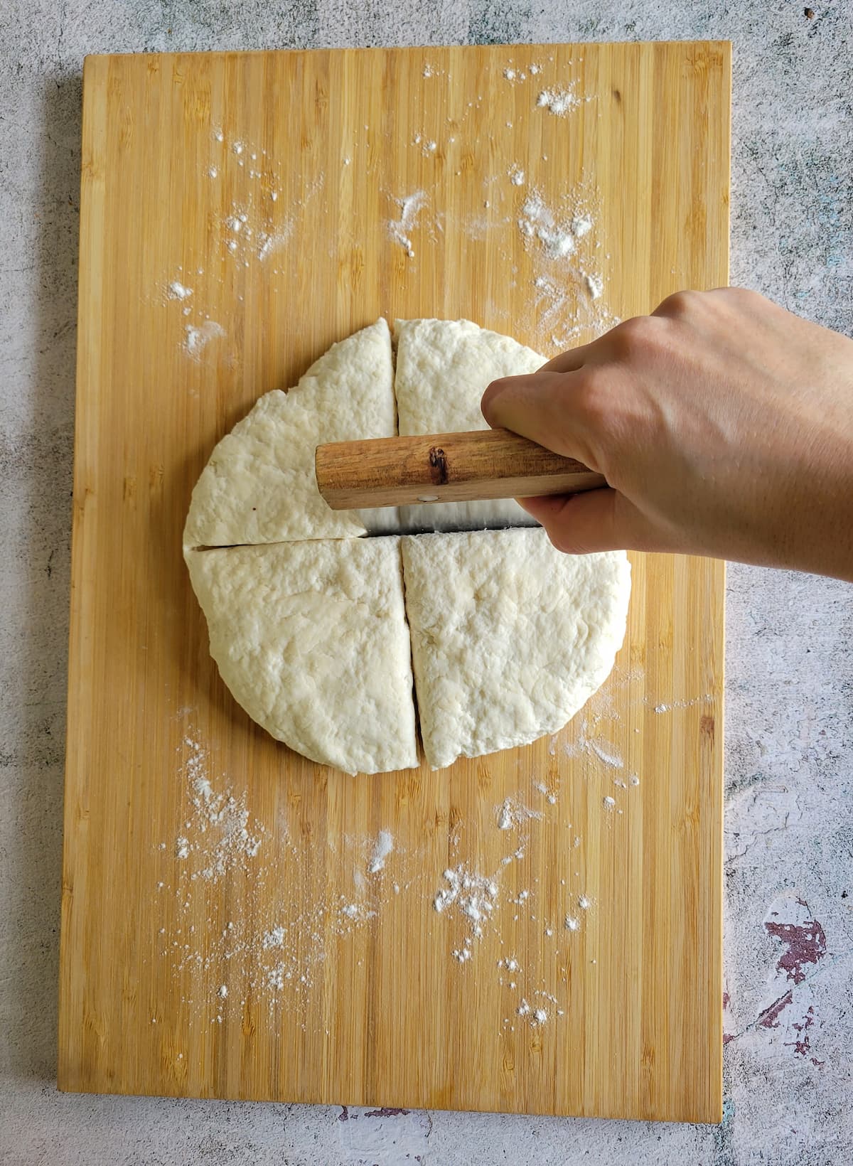 hand with a dough scraper cutting a piece of dough into triangles
