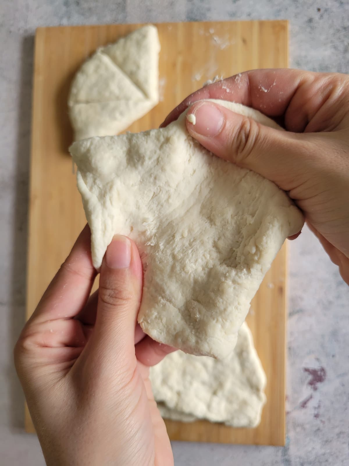 hand stretching a piece of dough over a cutting board with more pieces