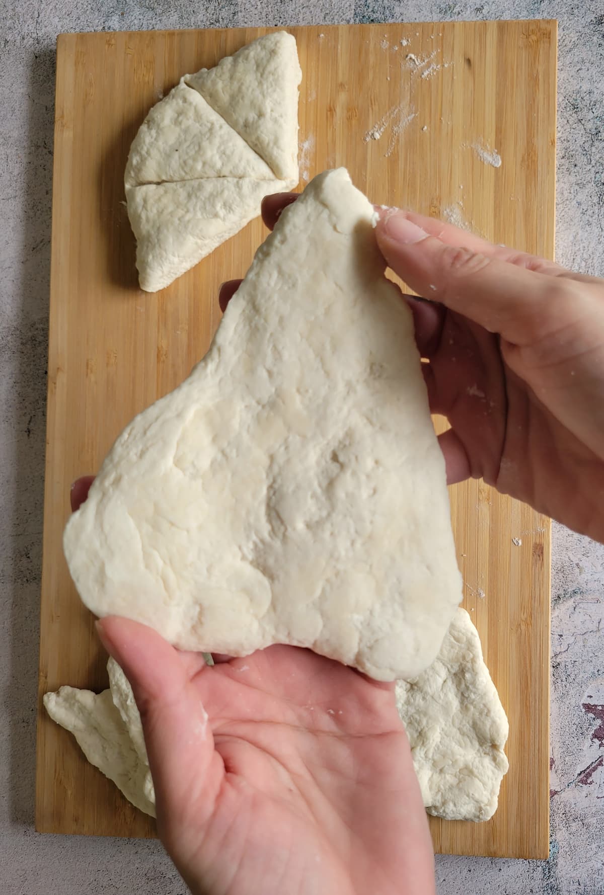 hands holding a triangular piece of dough over a cutting board with the rest of the dough pieces