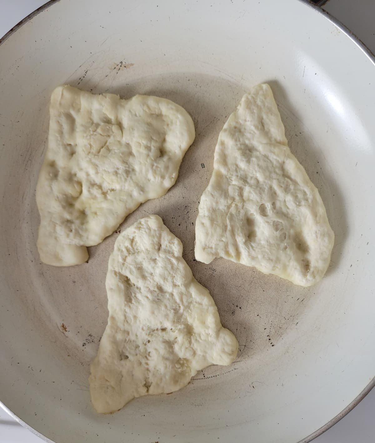 3 pieces of naan bread cooking in a skillet