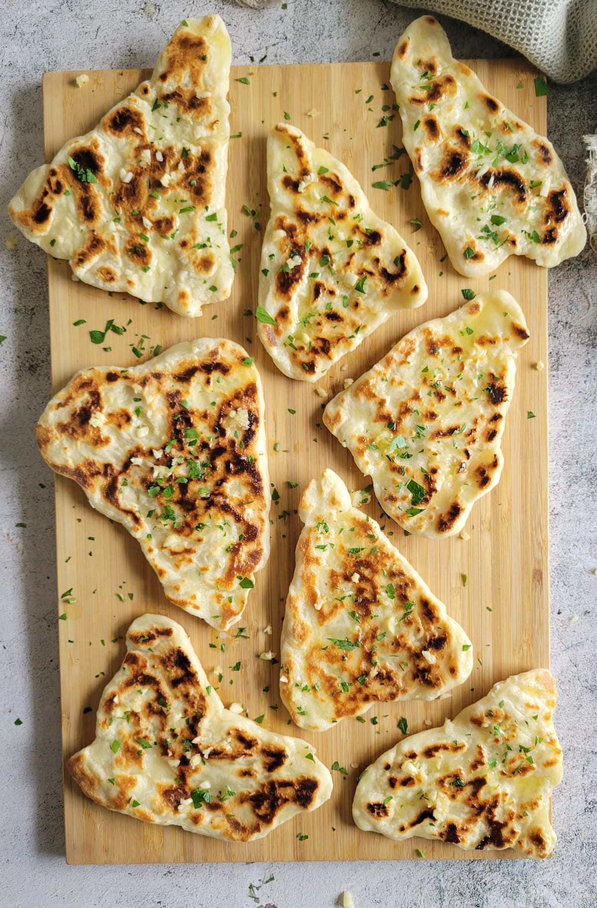 pieces of garlic naan garnished with fresh chopped parsley on a cutting board