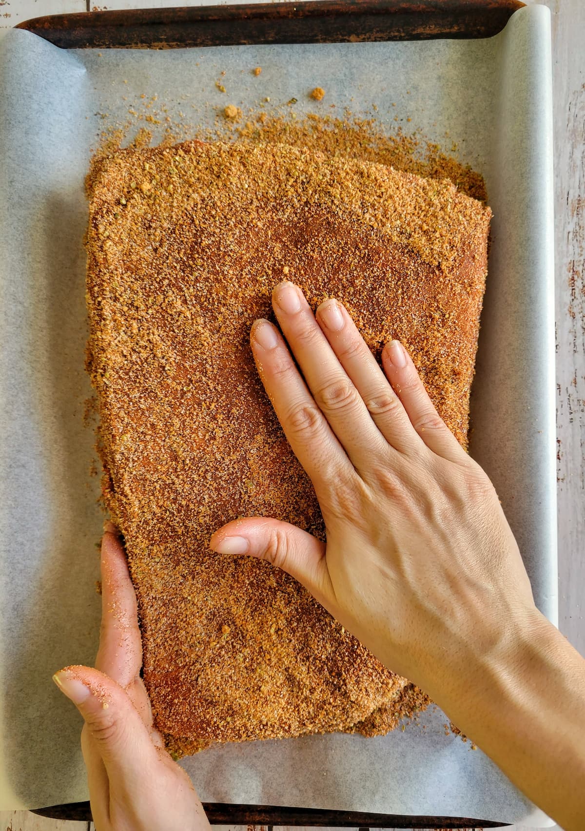 hand rubbing dry rub onto a whole raw brisket on a parchment lined baking sheet