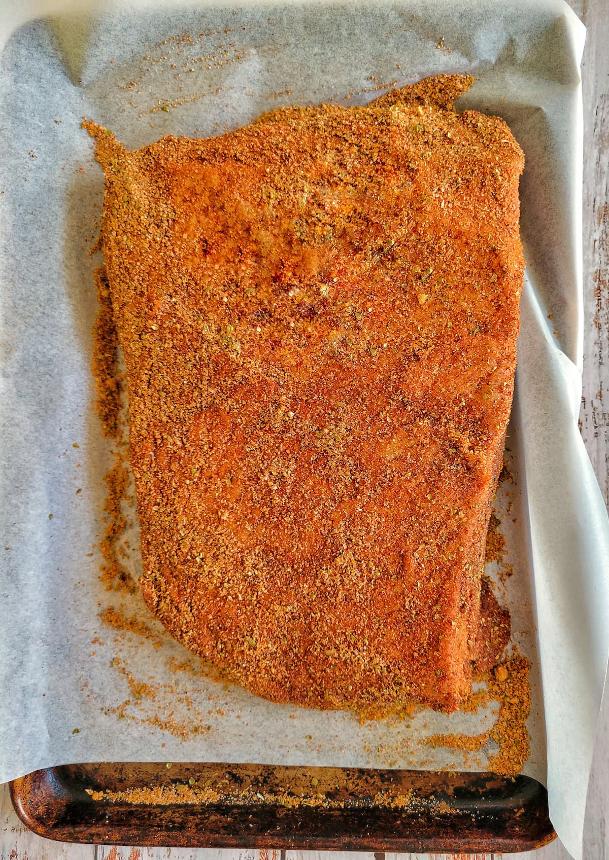 raw dry rubbed whole brisket on a parchment lined baking sheet
