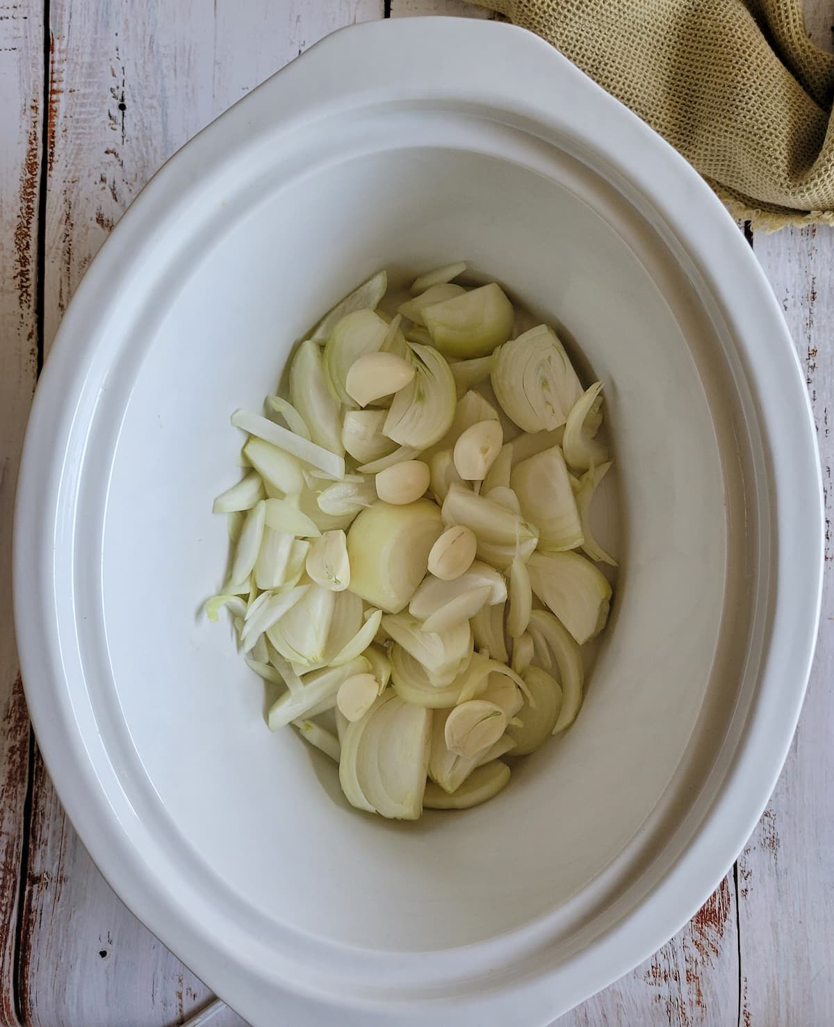 raw sliced white onions and whole peeled garlic cloves in a crockpot