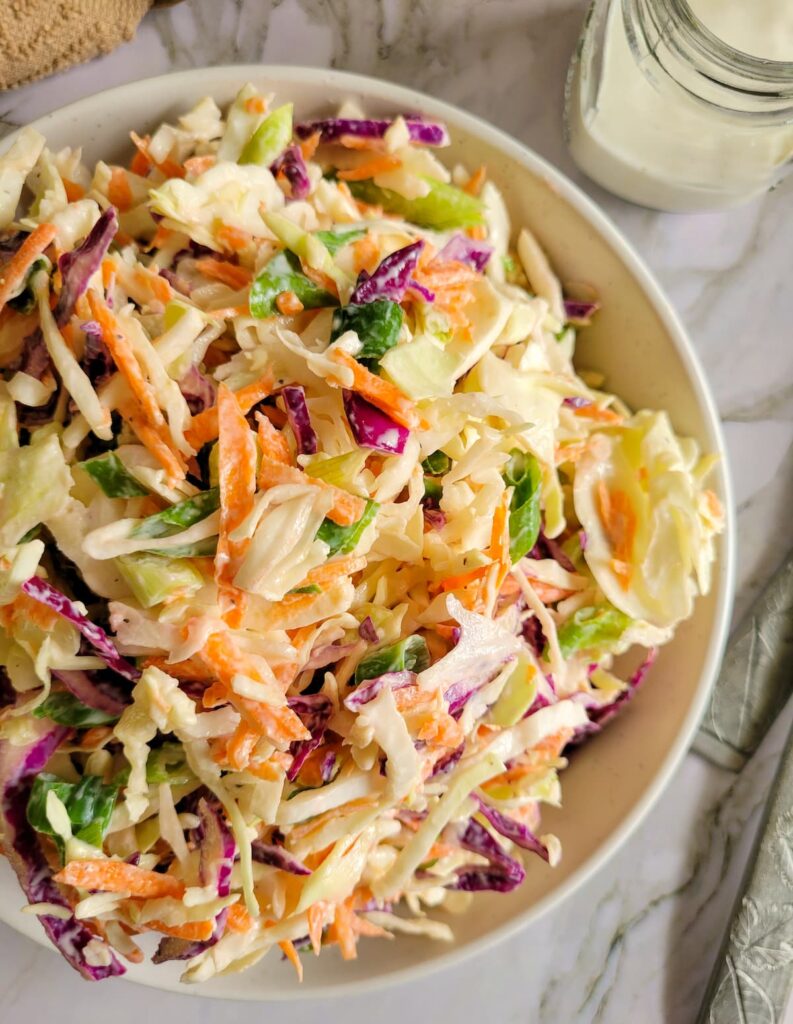bowl of creamy coleslaw, jar of dressing in the background