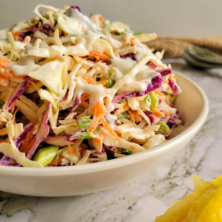 coleslaw piled high in a bowl topped with creamy dressing, lemon on the side
