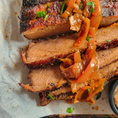 sliced brisket with onions and fresh herbs on a parchment lined baking sheet