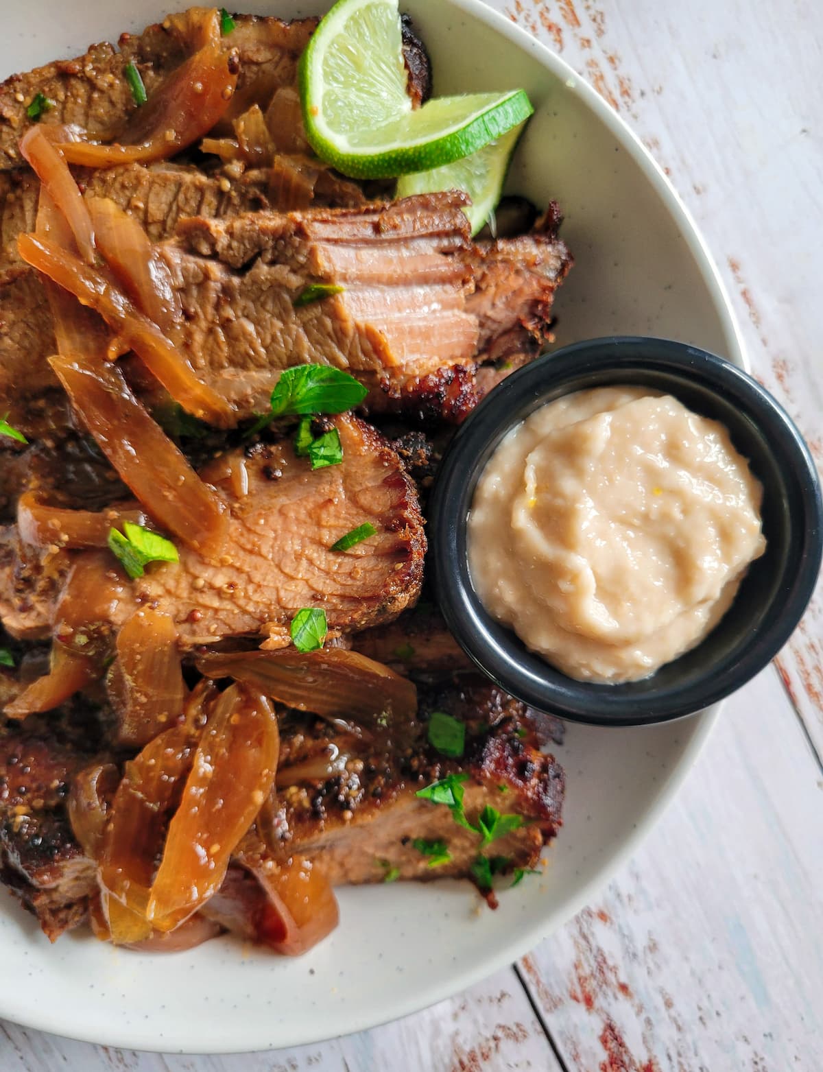 bowl of sliced brisket with fresh herbs, onions and lime, ramekin of horseradish in the bowl