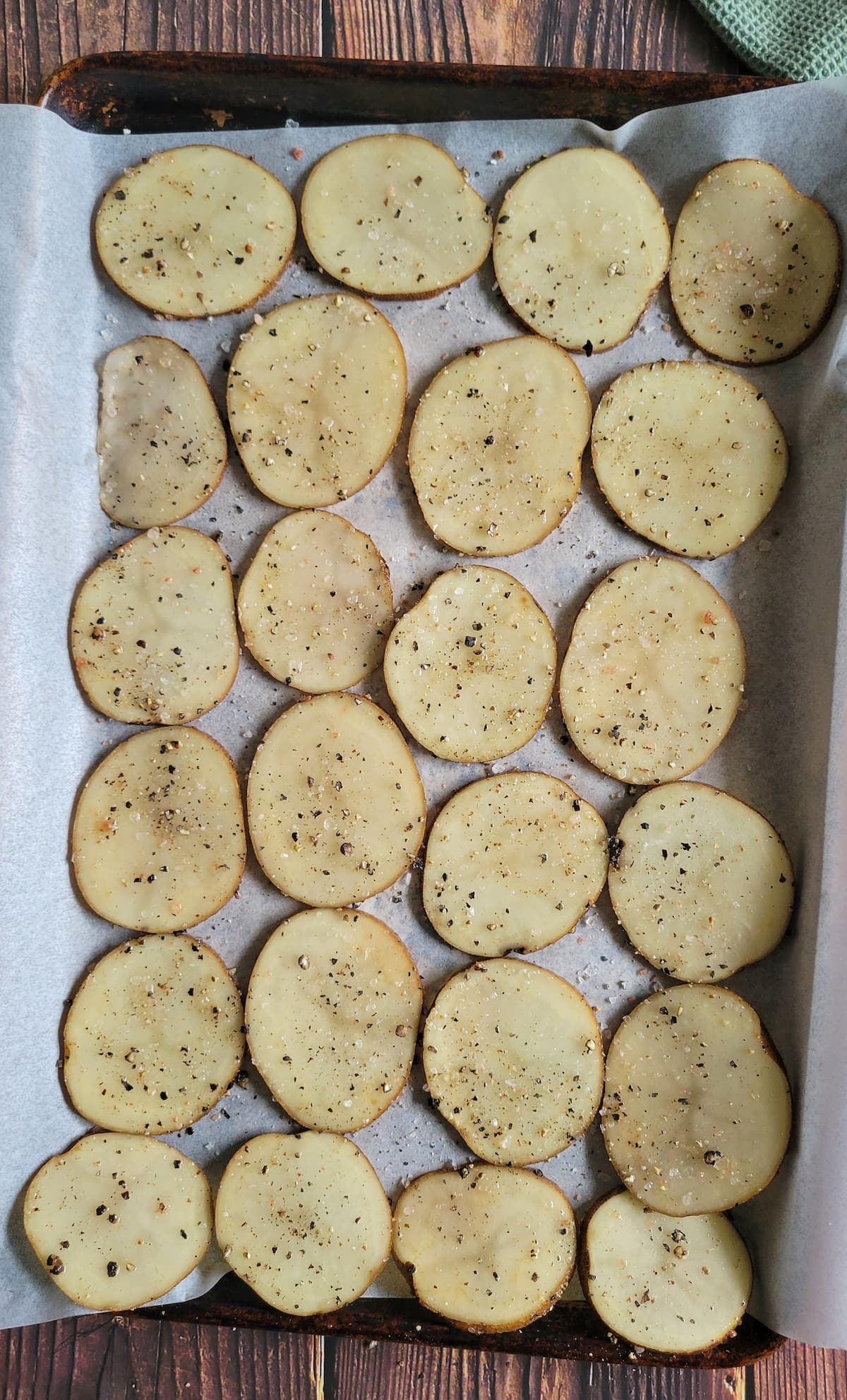 thinly seasoned sliced potatoes in a single layer on a parchment lined baking sheet