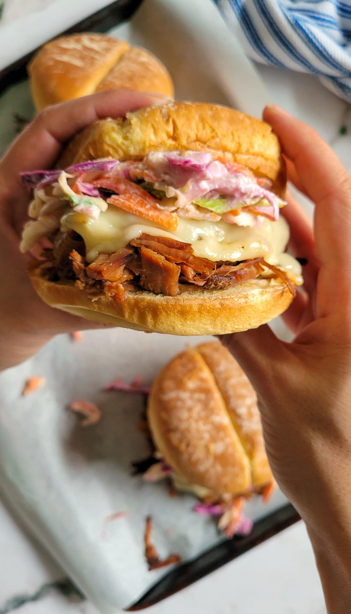 hand holding a sandwich with brisket of beef, cheese and coleslaw over a tray with more