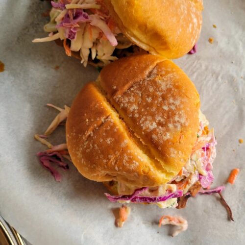 two brisket sandwiches with coleslaw on a parchment lined baking sheet