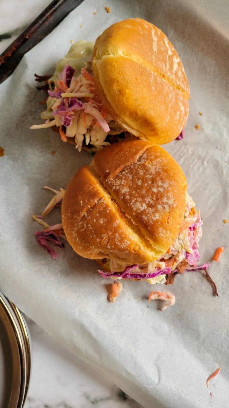 two brisket sandwiches with coleslaw on a parchment lined baking sheet