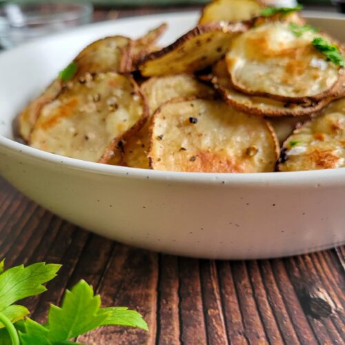 homemade potato chips in a bowl garnished with fresh chopped parsley