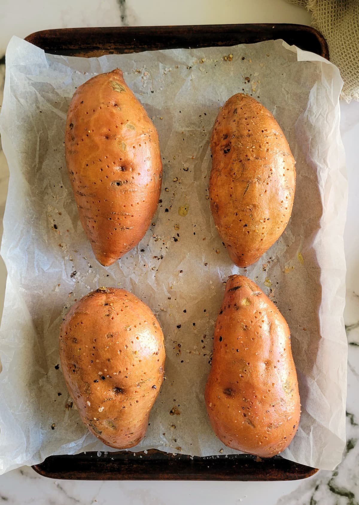4 sweet potatoes seasoned with salt and pepper on a parchment lined baking sheet