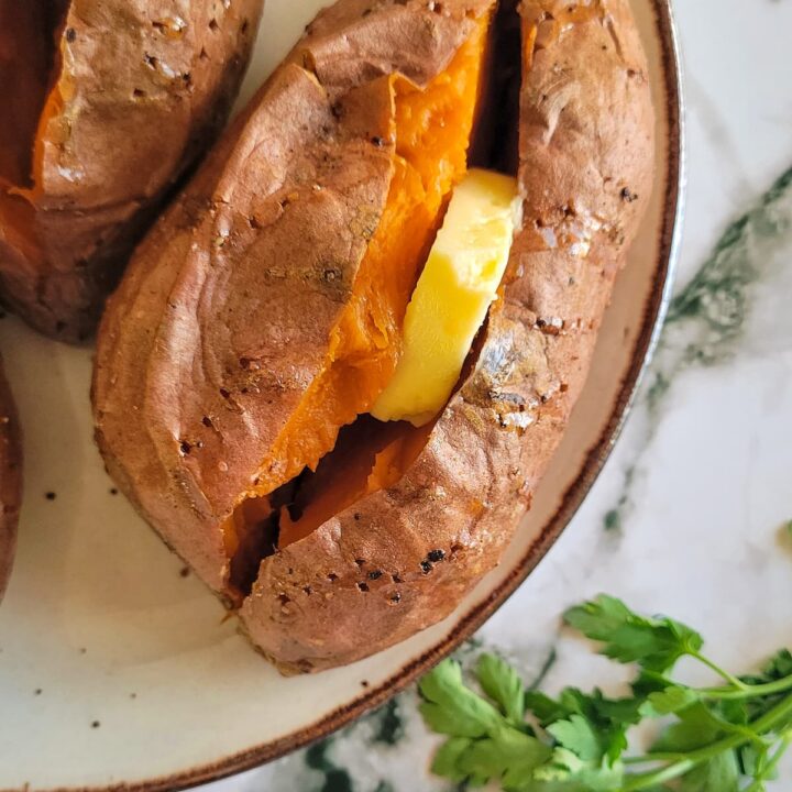 baked sweet potato cut open with a slice of butter, herbs in the background