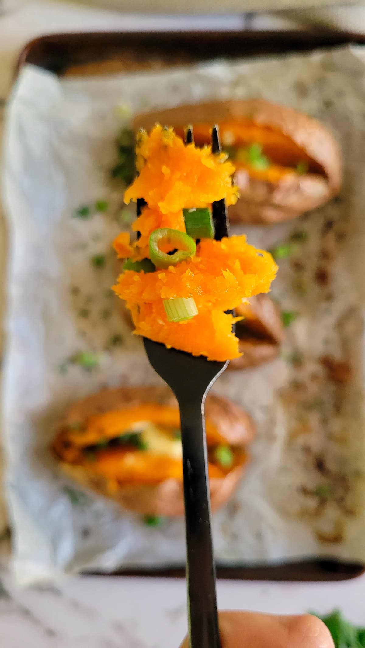 fork full of tender sweet potato and chives over a sheet pan with baked sweet potatoes