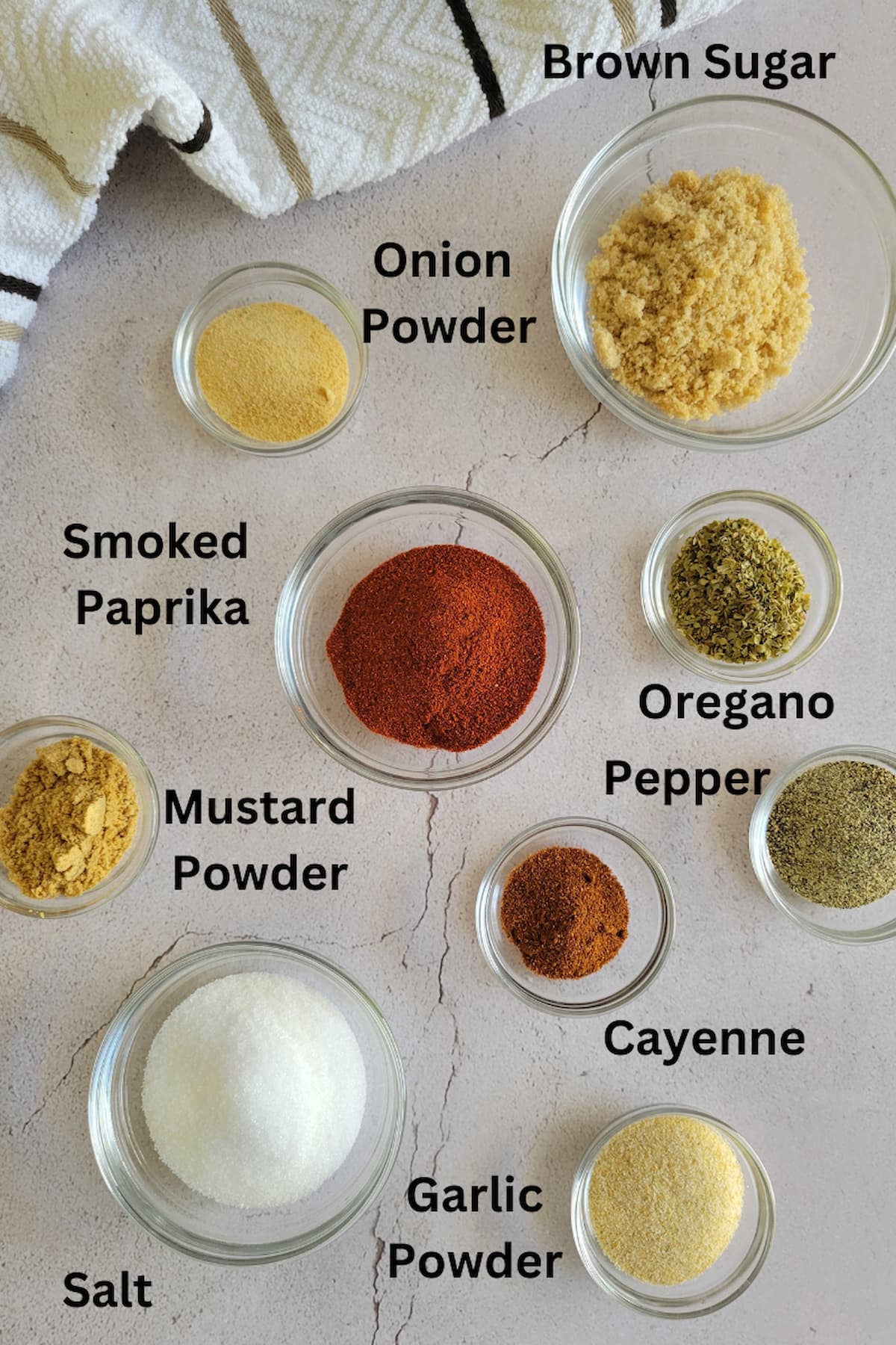 ingredients for recipe for brisket rub - mustard powder, onion powder, garlic powder, cayenne, salt, pepper, oregano, brown sugar, smoked paprika